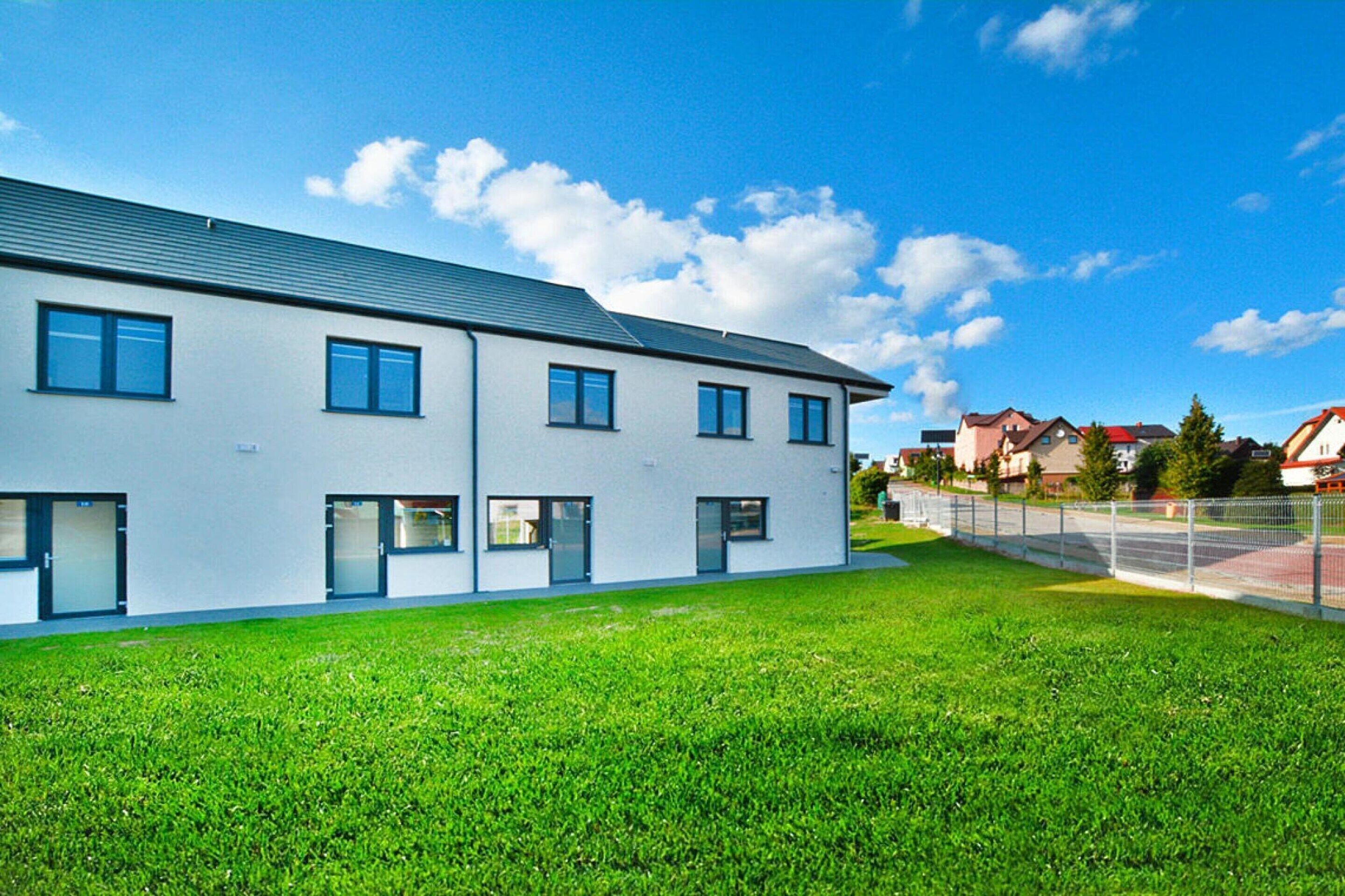 A modern building with multiple windows and a flat roof, surrounded by a well-maintained lawn.