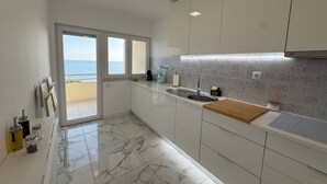 Une cuisine moderne avec vue sur la mer, des meubles blancs, un sol en marbre et un plan de travail en bois.