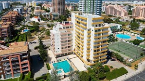 Un hôtel de grande hauteur doté de nombreux balcons, d’une piscine et d’un court de tennis.