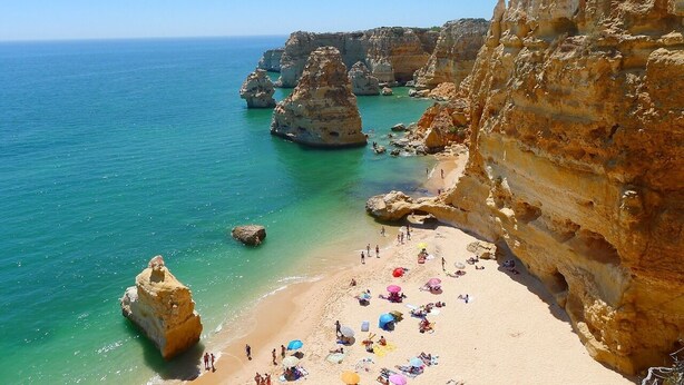 Une plage côtière bordée de falaises rocheuses et baignée d’une eau turquoise cristalline.
