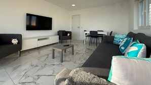 Un salon moderne doté d’un téléviseur à écran plat, d’un canapé, d’une table basse et d’un coin repas avec des chaises.