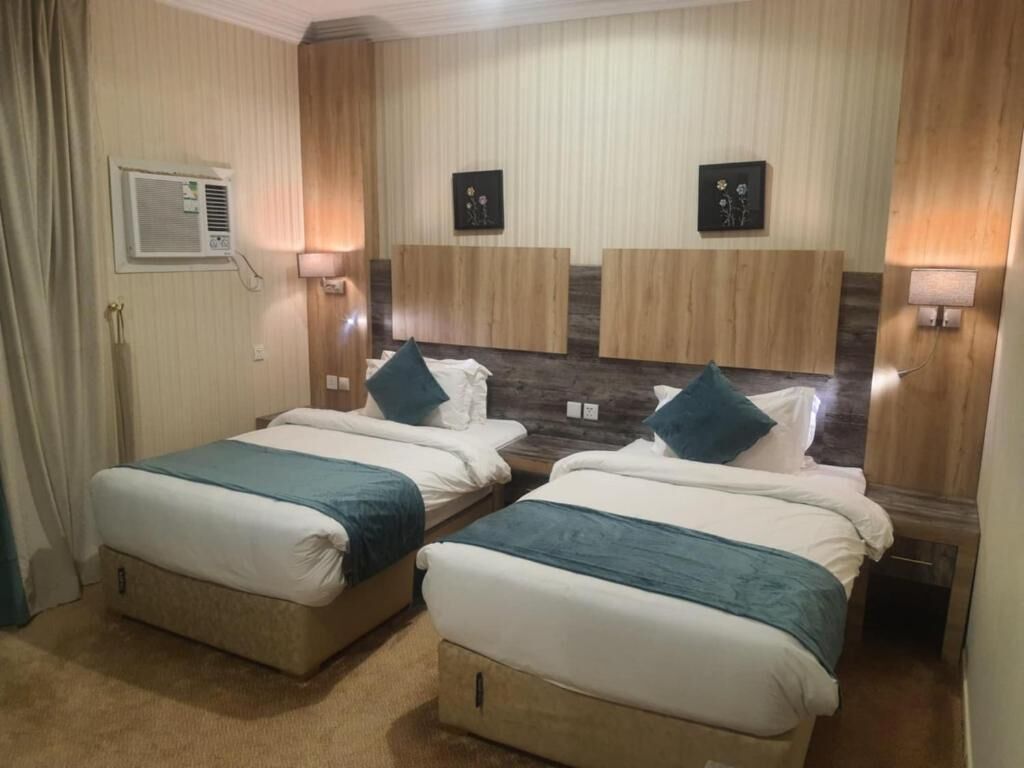Habitación de hotel con dos camas, cabecero de madera, aire acondicionado de pared y cuadros enmarcados.