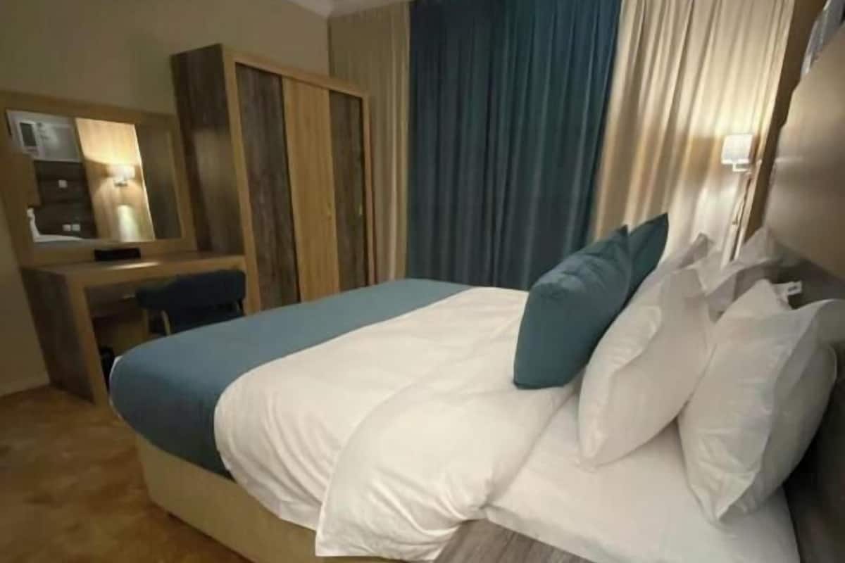 Una camera d'albergo con un letto, una scrivania, uno specchio e tende.