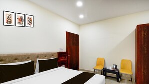 Camera d'albergo con un letto, due sedie, un tavolino e un bollitore, più una porta.