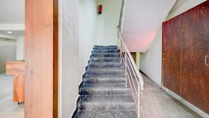 Una scala con ringhiera in metallo, un pilastro in legno e un estintore sulla parete.