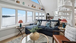 A living room with a large window, a dark blue sofa, a round coffee table, and a white staircase. - Book 2 homes together. Ocean Views. Sleeps 8! (Lunenburg)