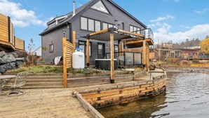 A house with a dock extending into a body of water, a covered outdoor seating area, and a water heater on the dock. - Book 2 homes together. Ocean Views. Sleeps 8! (Lunenburg)