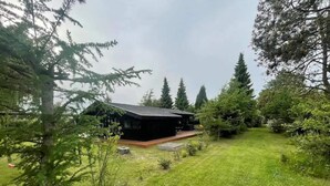 Una casa con techo inclinado, rodeada de un césped cuidado y altos árboles.