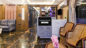 A hotel lobby with a reception desk, a sofa, wicker chairs, a marble floor, and a modern ceiling light. - Super Townhouse Aiims Kolkata (Kalyani)