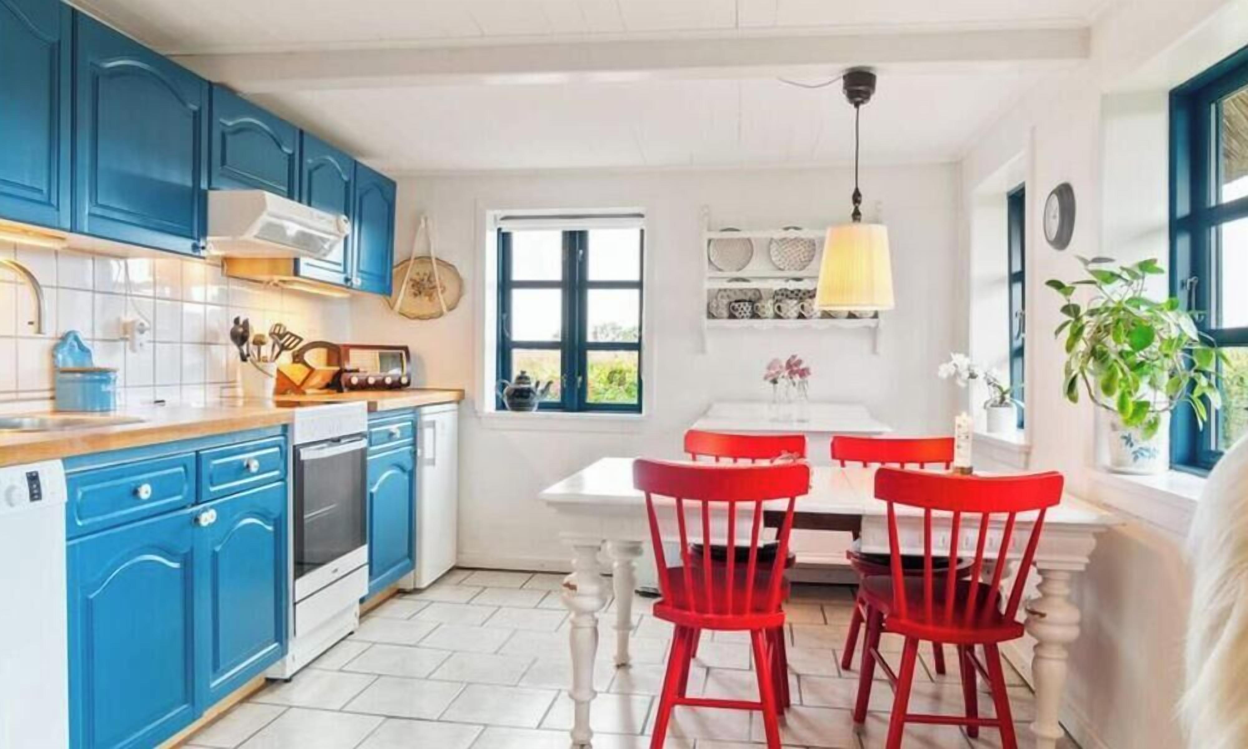 Cozinha com armários azuis, bancada branca e conjunto de jantar vermelho.