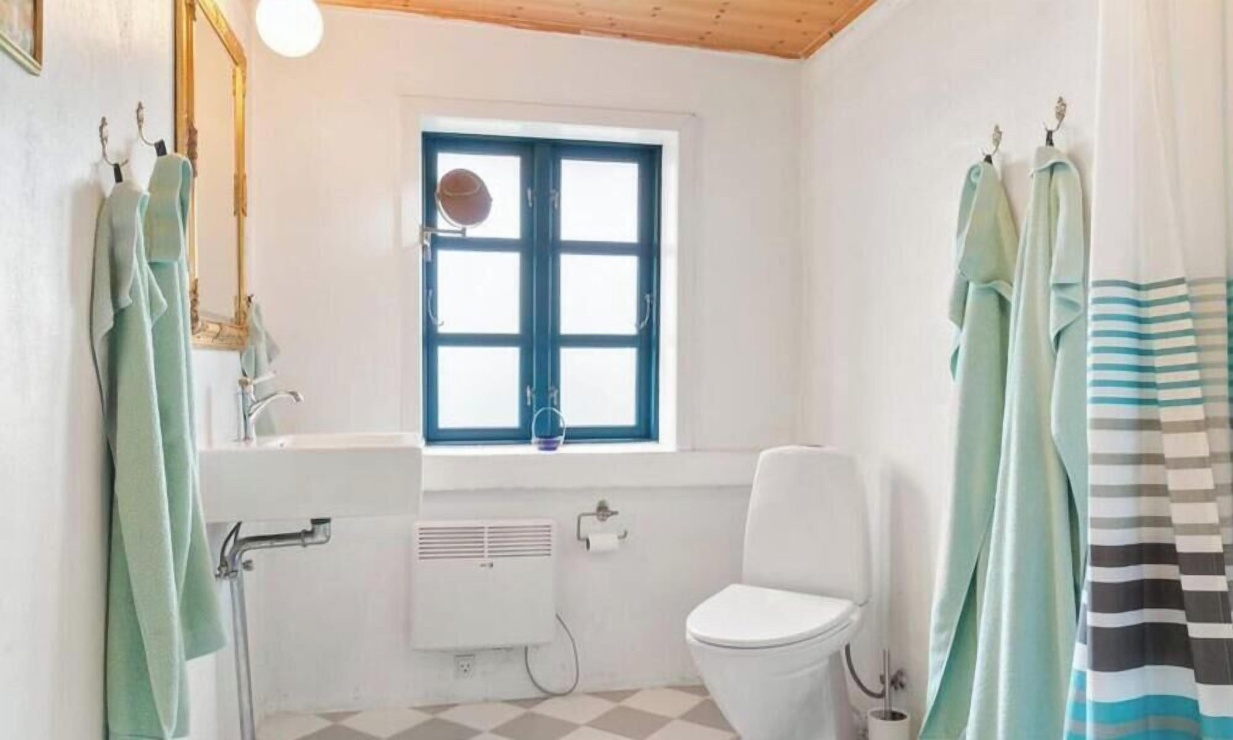 Une salle de bain avec des toilettes blanches, une fenêtre avec des volets bleus, un lavabo et un porte-serviettes.