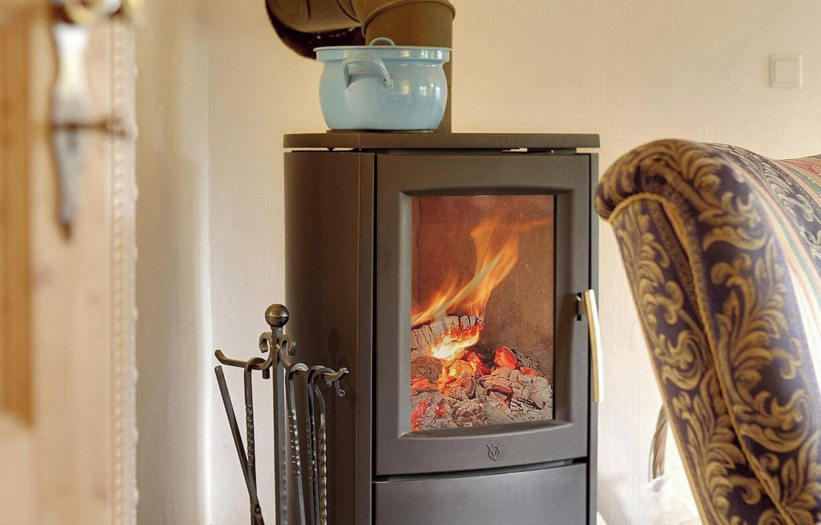 Un poêle à bois avec une porte en verre, une casserole posée sur le dessus et une chaise au premier plan.