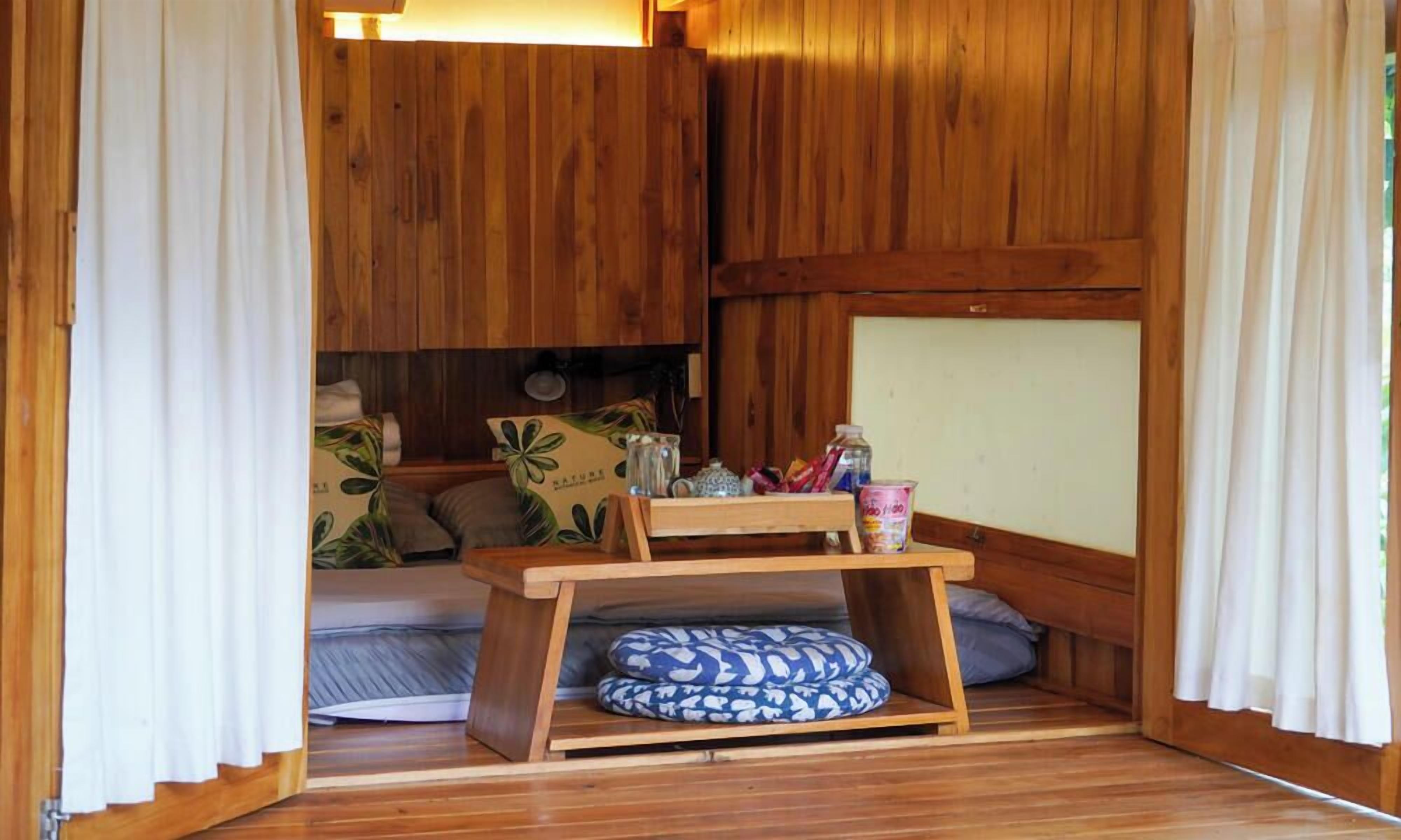 A cozy room with a bed, a small table, and a shelf with various items.
