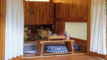 A cozy room with a bed, a small table, and a shelf with various items.