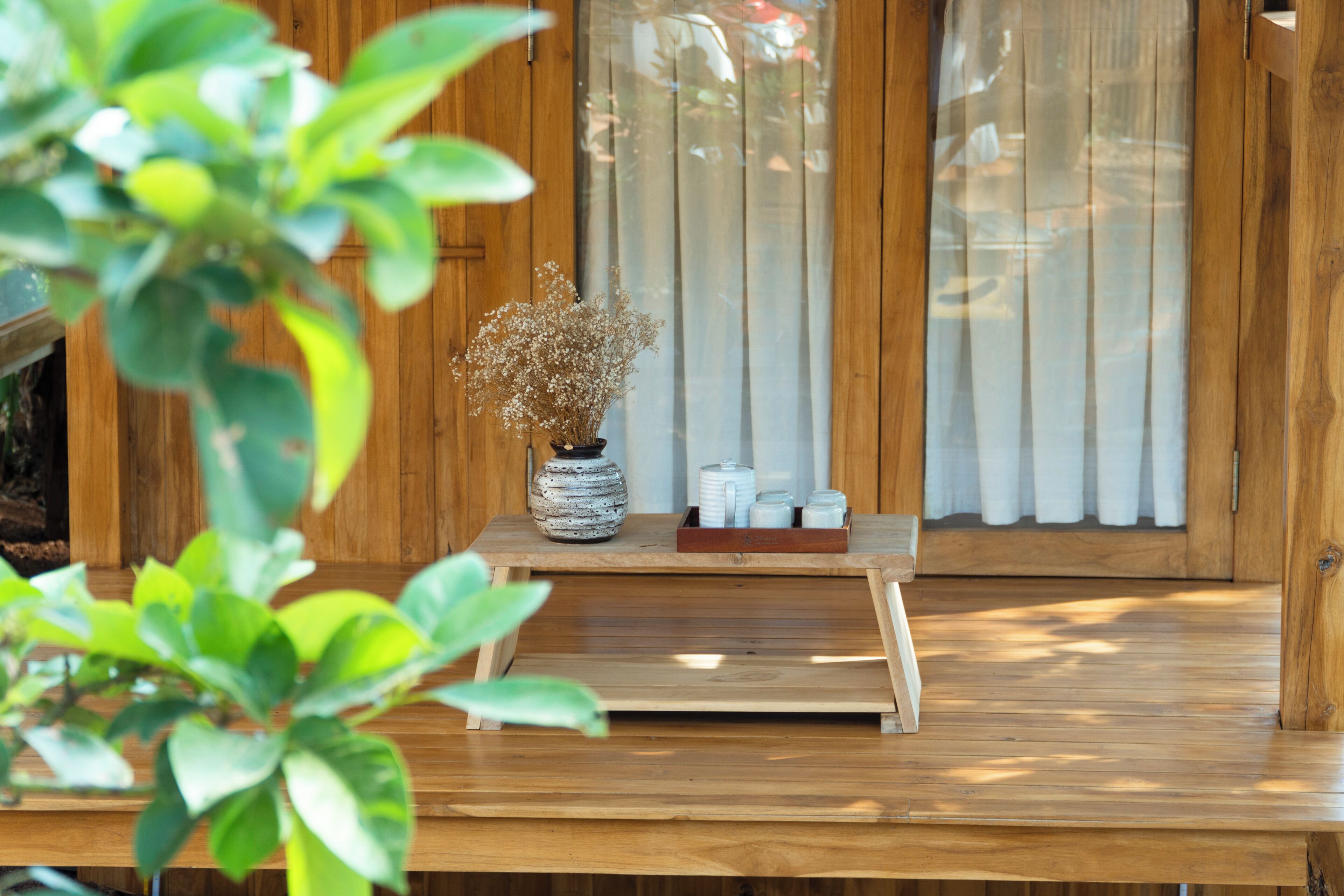 A wooden table with a vase of dried flowers and a tray of white teapots.