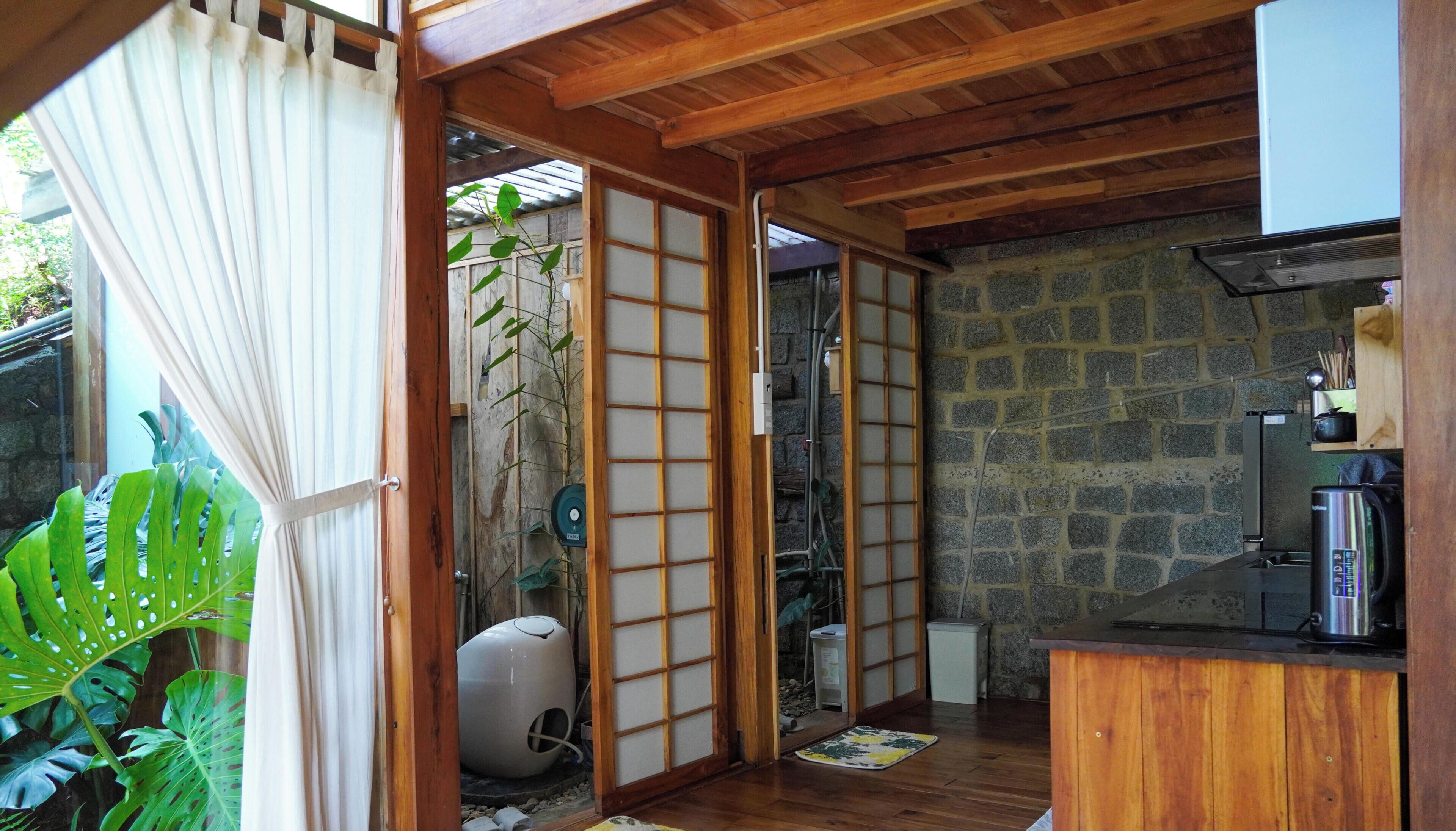 A traditional Japanese-style room with tatami flooring, a stone wall, a wooden ceiling, and a sliding door with shoji screens.