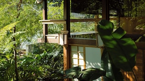 A traditional wooden structure with large windows, surrounded by lush greenery.