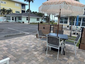 Un espace patio avec des sièges d’extérieur, un parasol à motifs et une vue sur un immeuble doté d’un balcon.