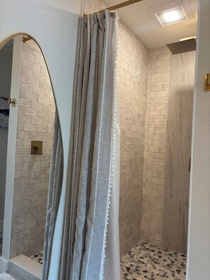 Une douche avec un rideau, un mur carrelé et un luminaire.