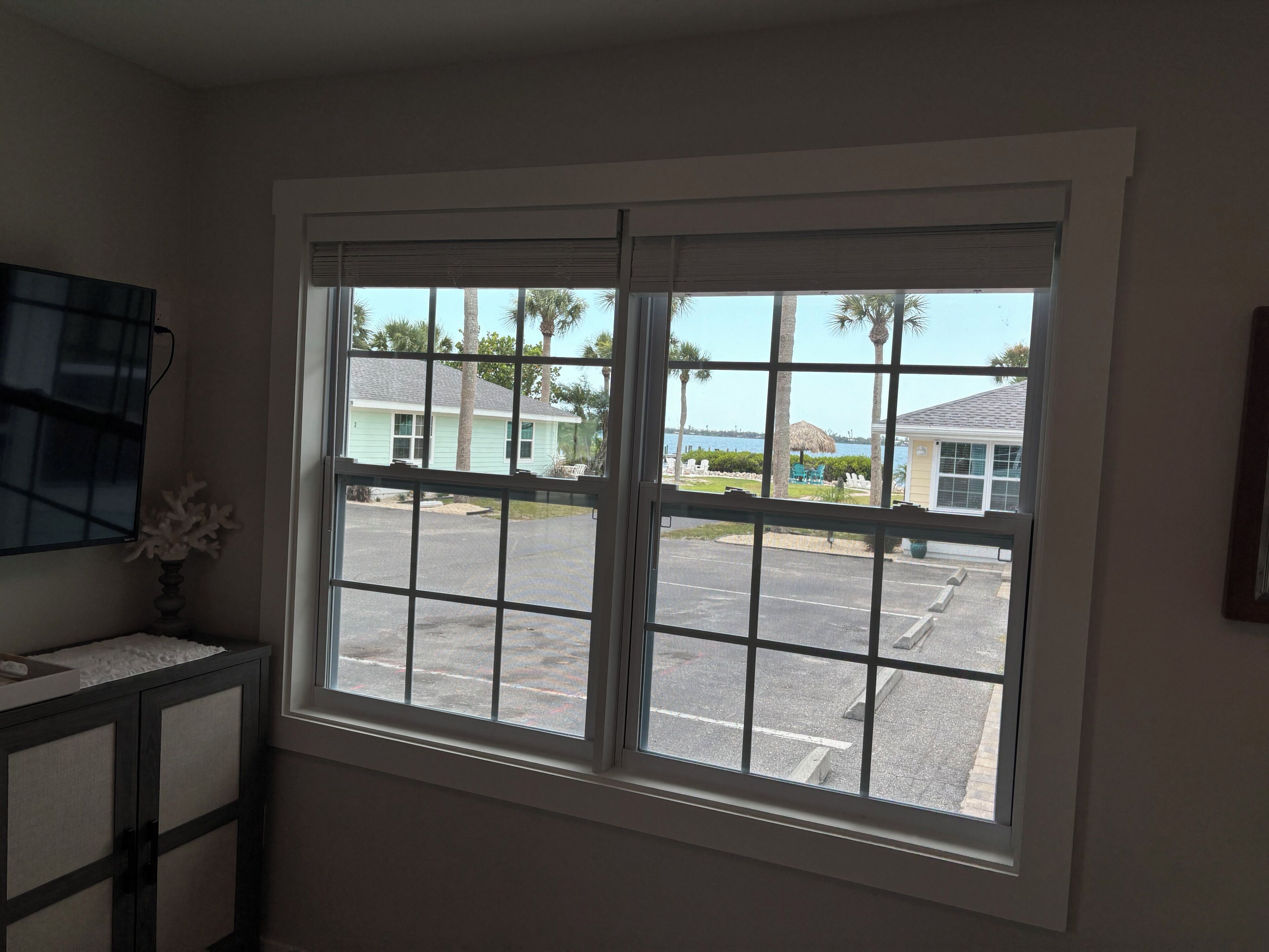 A room with a large window, a flat-screen TV, and a small cabinet.