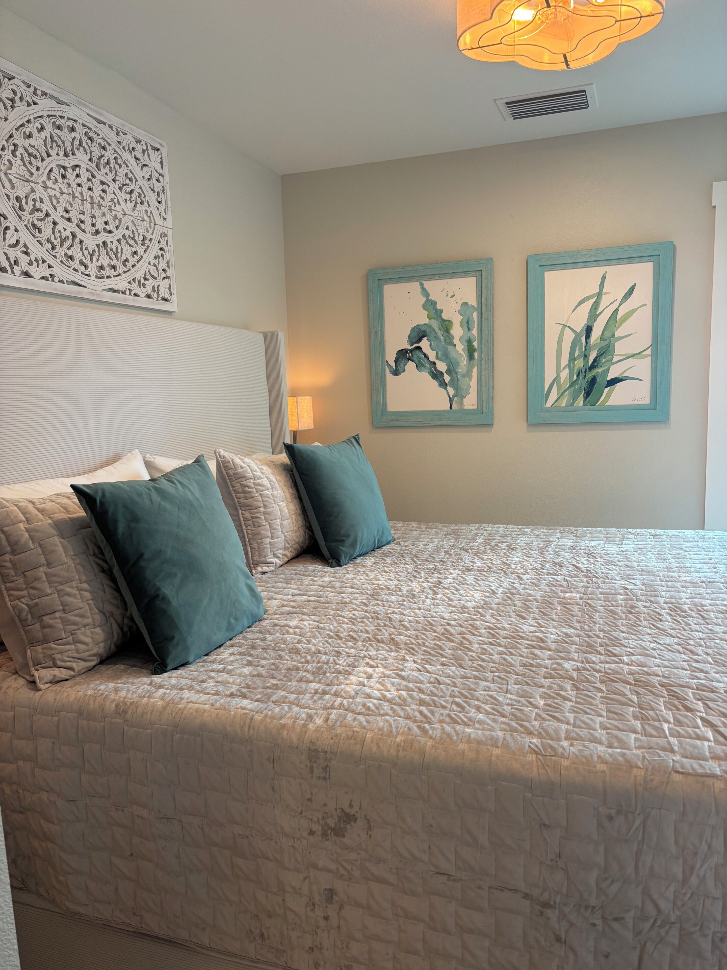 Une chambre à coucher avec un lit, des oreillers, une tête de lit, des œuvres d’art murales et un luminaire au plafond.