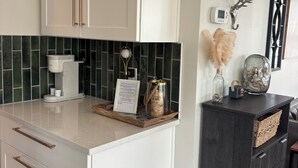 Una cocina con armarios blancos, una cafetera, un menú enmarcado, elementos decorativos y un mueble de madera oscura.