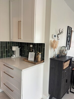 Eine Küche mit weißen Schränken, einer Kaffeemaschine, einer gerahmten Speisekarte, Dekoration und einem dunklen Holzschrank.