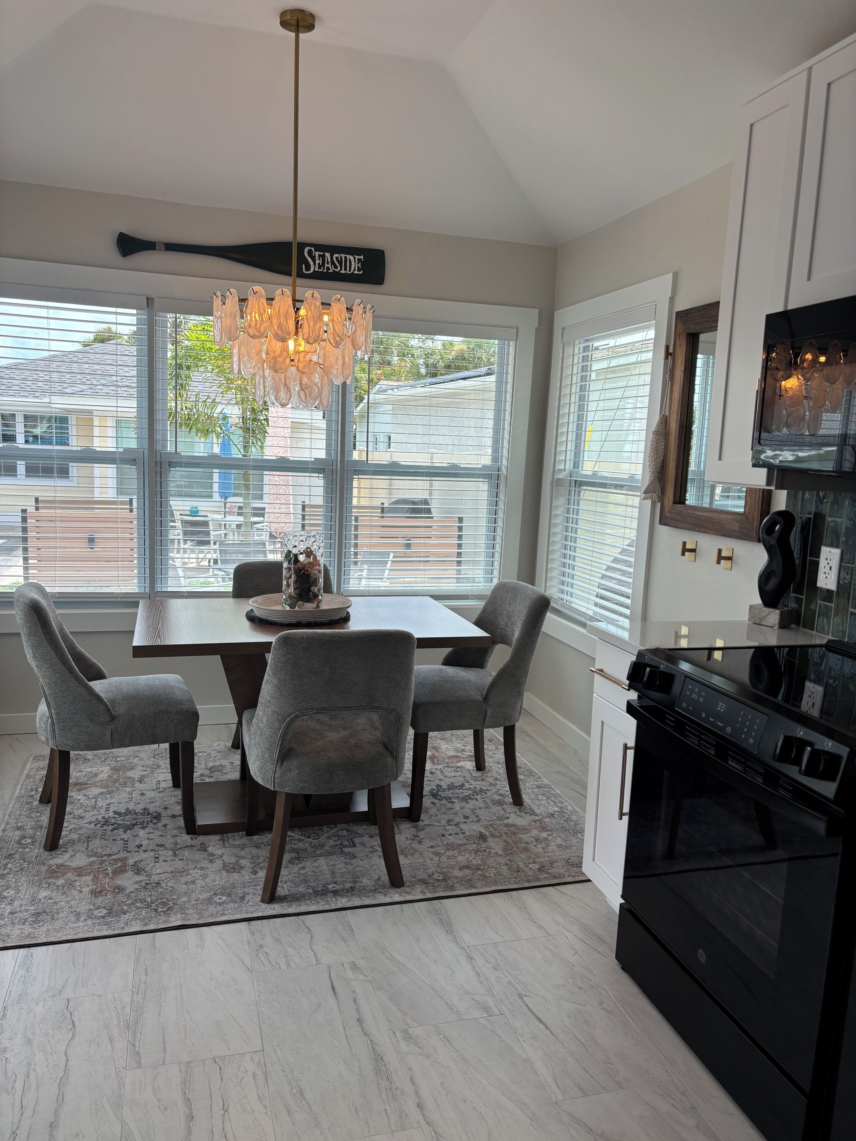 A modern kitchen with a dining area, large windows, and a chandelier.