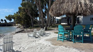 Un entorno costero con una estructura de techo de paja, zona de estar y palmeras.