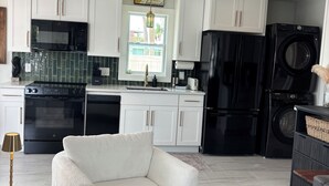 Una cocina moderna con armarios blancos, un refrigerador negro, una lavadora y un sillón blanco.