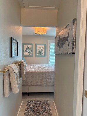 A bedroom with a bed, a hanging towel rack, a rug, and wall art. - 7th Heaven is Yours to Discover at Tiki On The Bay (Englewood)