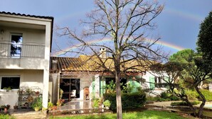 Ein Wohngebäude mit Ziegeldach, ein Garten mit einem Baum und ein sichtbarer Regenbogen.