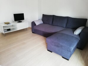 A modern living room with a sectional sofa, a flat-screen TV, and a white entertainment unit. - Gd Appartement 74 M2  1300 m plages (Le Pradet)