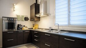 A modern kitchen with dark cabinetry, a stainless steel oven, a coffee maker, and a window with blinds.