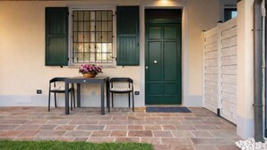 A patio with a table and chairs, a green door, and a window with shutters.