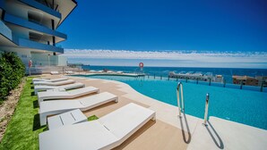 Een modern hotel met een zwembad, ligstoelen en uitzicht op zee.