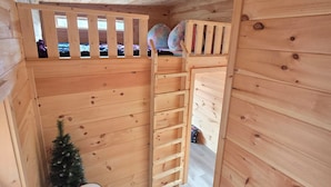 A wooden cabin interior with a loft bed, a small Christmas tree, and a white table.