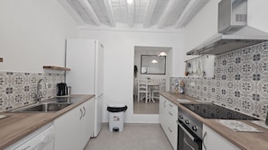 Ett kompakt kök med vita skåp, en träbänkskiva, en inbyggd ugn och ett kylskåp.