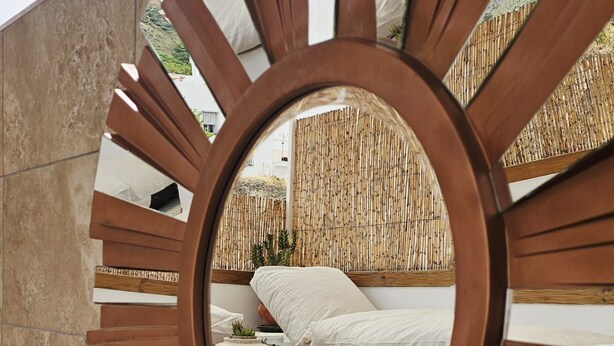 Eine runde Holzkonstruktion mit spiegelnder Oberfläche, einem Bett mit weißer Bettwäsche und einem Bambuszaun im Hintergrund.