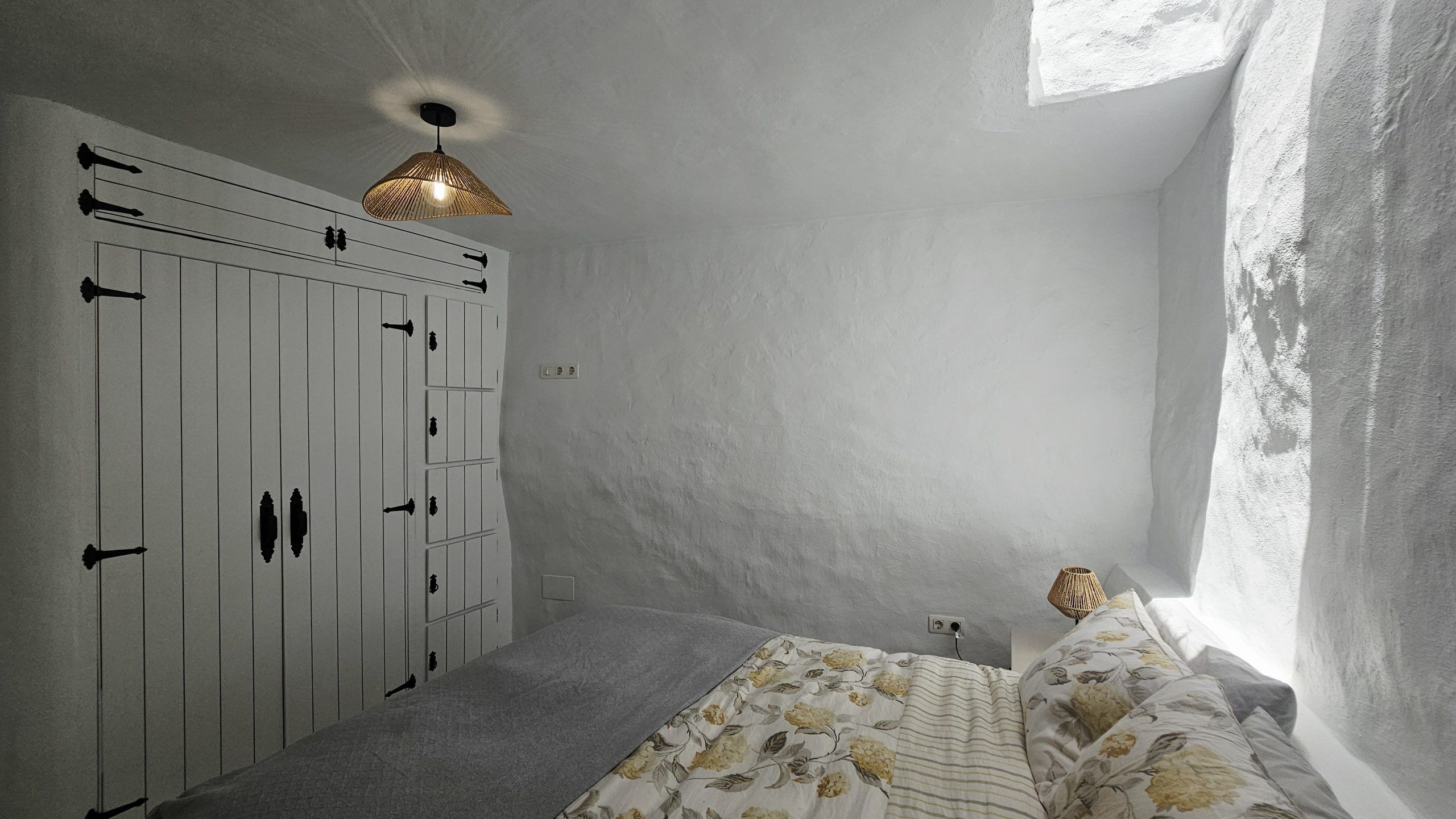 A bedroom with a bed, a wardrobe, a hanging light fixture, and a window.