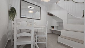 Ein weißes Zimmer mit einem runden Tisch, Stühlen, einer hängenden Pflanze, einem Spiegel und einer Treppe.