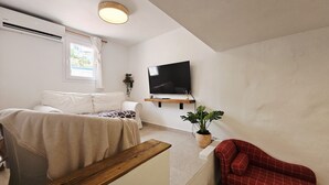 Ein Schlafzimmer mit einem Bett, einem an der Wand montierten Fernseher, einem Fenster mit Vorhängen, einer Zimmerpflanze und einem roten Sessel.