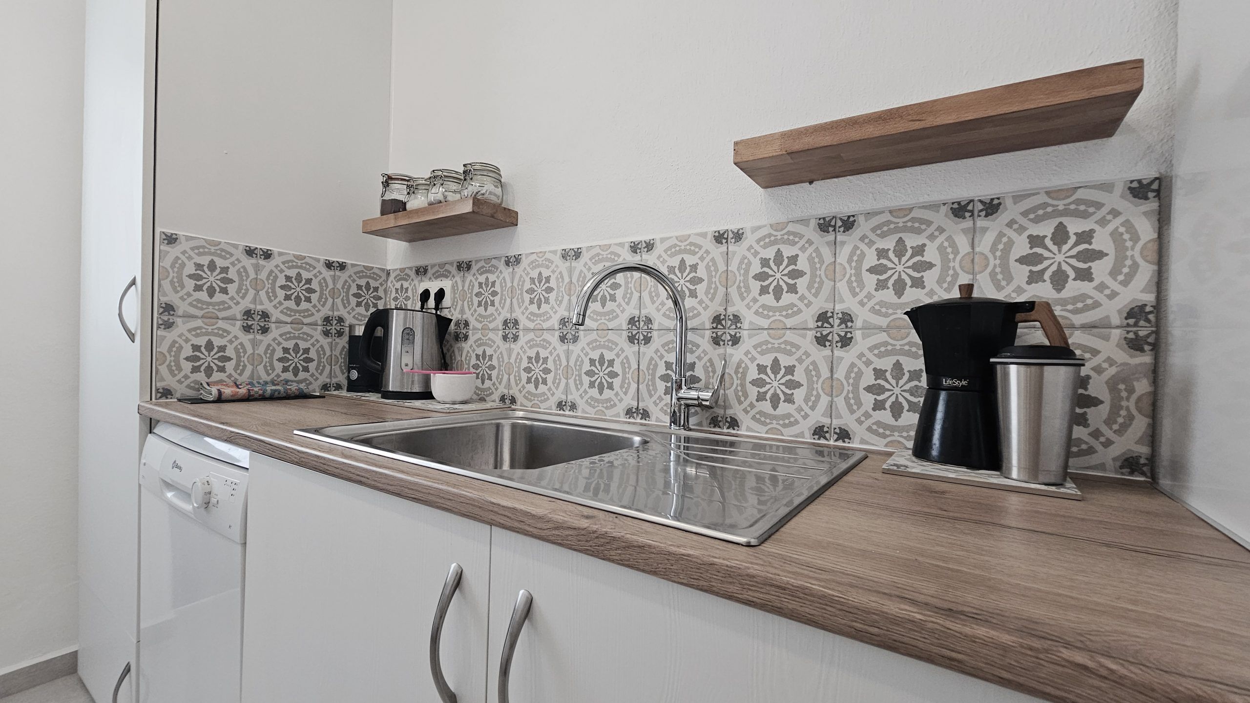 A kitchen with a stainless steel sink, a coffee maker, and a kettle on the countertop.