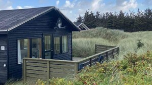 A small cabin with a deck, surrounded by tall grass and trees. - 4 Star Holiday Home in Lokken (Lokken)