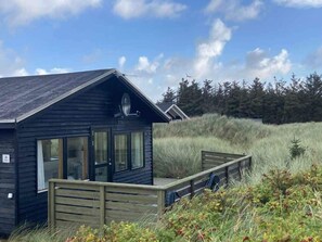 A small cabin with a deck, surrounded by tall grass and trees. - 4 Star Holiday Home in Lokken (Lokken)