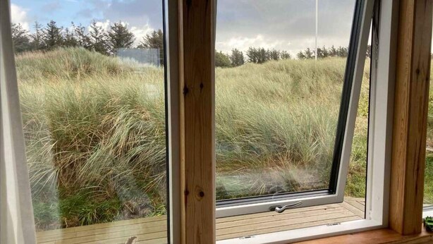 A room with a large window overlooking a grassy field and trees. - 4 Star Holiday Home in Lokken (Lokken)