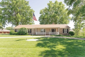 Ein zweistöckiges Haus mit Veranda, Fahnenmast und amerikanischer Flagge sowie einem gepflegten Rasen.
