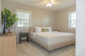 Un dormitorio con cama, ventilador de techo, mesita de noche, planta y cómoda.