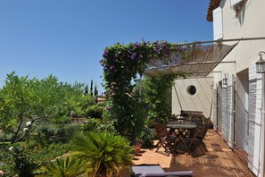 A patio with a table and chairs, surrounded by potted plants and a pergola with flowers. - Entre mer et garrigue - Charming house with pool and sea view in Provence (LA CADIERE D'AZUR)