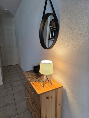 Eine Holzkommode mit einer Lampe, ein Spiegel an der Wand und ein Fliesenboden.